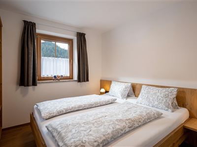 Een gezellige slaapkamer met een tweepersoonsbed en twee nachtblokken. Het raam laat zacht licht binnen en biedt een uitzicht naar buiten.