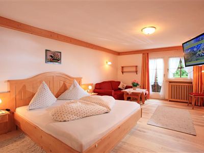 Een uitnodigende slaapkamer met een groot bed en een gezellige zithoek. Heldere kleuren en houten details creëren een warme sfeer.