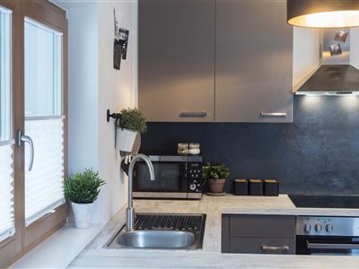 Een moderne keuken met grijze kasten en een werkruimte van steen. Planten decoreren de vensterbank en de werkoppervlakken.