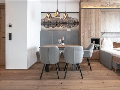 Een moderne eetkamer met een houten tafel en grijze stoelen. Boven de tafel hangen elegante lampen en de muren zijn van licht hout.