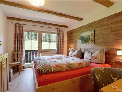 Ein gemütliches Schlafzimmer mit einem Doppelbett und rustikaler Holzverkleidung. Durch die Fenster blickt man auf eine grüne Landschaft.