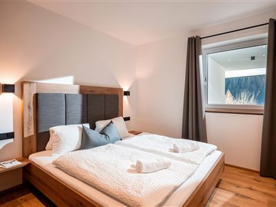 Ein modernes Schlafzimmer mit einem gemütlichen Doppelbett und Holzfußboden. Durch das Fenster ist eine wunderschöne Aussicht auf die Natur sichtbar.