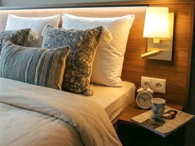 A cozy bedroom with a large bed and decorative cushions. On the nightstand are a cup and a magazine.