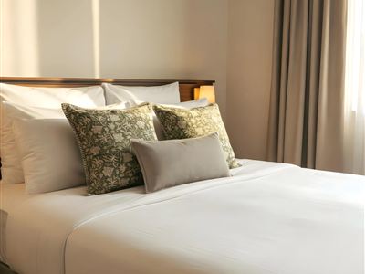 A cozy bedroom with a large bed and decorative pillows. Soft light falls through the window, creating an inviting atmosphere.