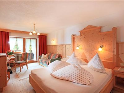 Een gezellige kamer met houten meubels en een groot tweepersoonsbed. Er is een zithoek en veel daglicht door de ramen.