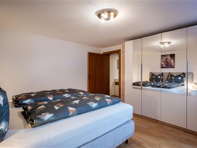 Ein modernes Schlafzimmer mit einem Doppelbett und einem großen Spiegel. Die Wände sind hell und der Boden ist aus Holz.