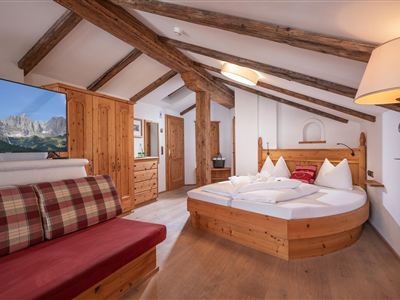 A cozy room with wood paneling and a round bed. There is a couch and a beautiful view of the mountains.
