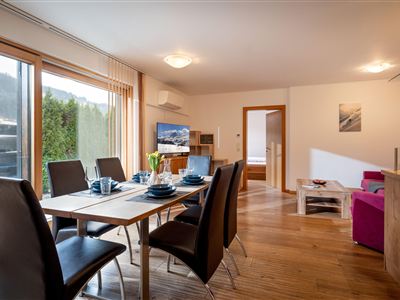 Ein modernes Wohnzimmer mit einem Esstisch und eleganten Stühlen. Große Fenster bieten viel Licht und einen Blick ins Freie.