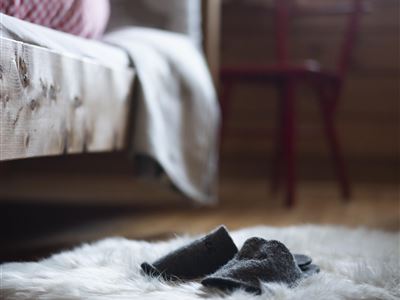 Et hyggeligt soveværelse med en træseng og en rød stol. På et blødt tæppe ligger grå hjemmesko.