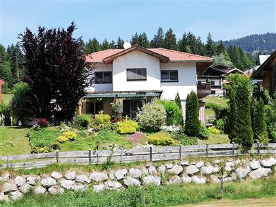 A modern house in a beautiful garden landscape. Surrounded by trees and mountains, it radiates a tranquil atmosphere.