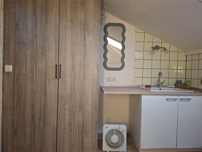 A small kitchen with wooden cabinets and a sink. A decorative mirror hangs on the wall.