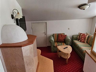 Een gezellige woonkamer met een bank en een fauteuil. De kamer heeft een rood tapijt en een rustieke kachel.