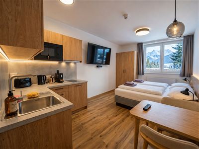 Een moderne kamer met een kleine kitchenette, een tafel en een bed. De ramen bieden uitzicht op de bergen.