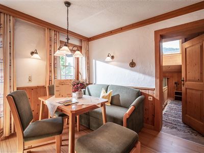 Een gezellige eetruimte met houten meubels en warm licht. Op de achtergrond is een open deur die naar een gang leidt.