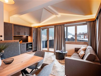Eine moderne Wohnung mit einem hellen Wohnbereich und großen Fenstern. Der Raum ist mit einem gemütlichen Sofa und einem Esstisch ausgestattet, umgeben von stilvollem Holzinterieur.