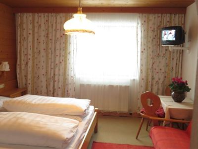 A cozy bedroom with two beds and wooden walls. There is a table, a chair, and a television in the room.