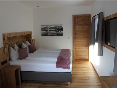 Ein modernes Schlafzimmer mit einem Doppelbett, Holzverkleidung und sanften Farben. Große Fenster lassen viel Tageslicht herein, und ein gemütlicher Schrank vervollständigt den Raum.