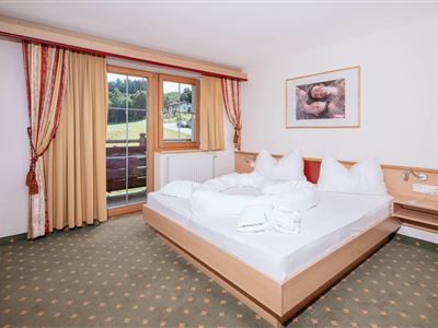 Ein gemüdliches Schlafzimmer mit einem großen Bett und weißen Bettdecken. Durch das Fenster ist die grüne Landschaft sichtbar.