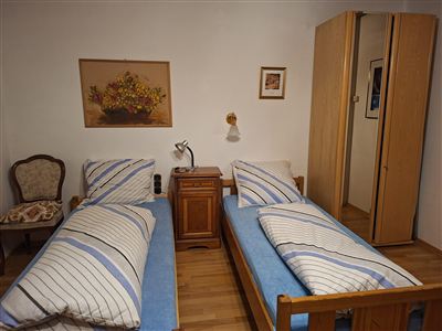 Ein einfaches Schlafzimmer mit zwei Einzelbetten und einer gemütlichen Ecke. An der Wand hängen Bilder, und es gibt einen Kleiderschrank.