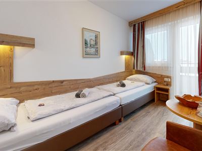 A cozy room with two single beds and wooden elements. The window is decorated with curtains and there is a small table with chairs.