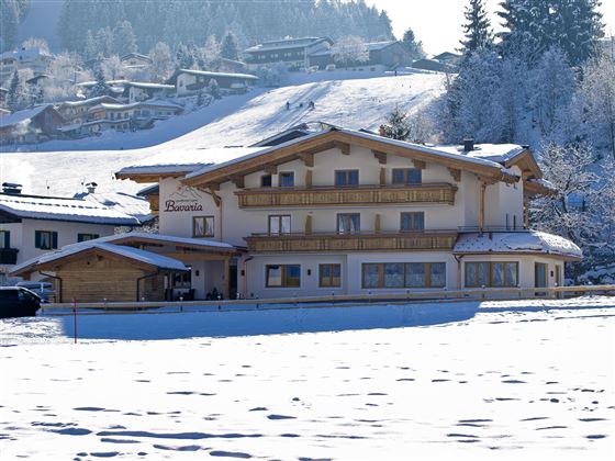 Ein malerisches Chalet im Winter, umgeben von Schnee und Bergen. Das Gebäude hat Holzverkleidungen und große Fenster.