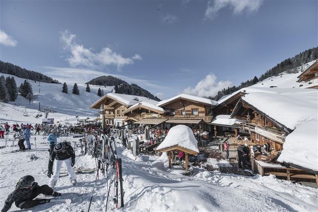 Ein malerisches Bergdorf mit Holzchalets im Schnee. Skifahrer genießen die winterliche Landschaft und die klaren Himmel.