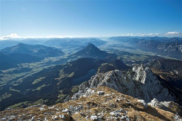 Ein beeindruckender Blick auf eine Berglandschaft mit grünen Tälern und blauem Himmel. Die Felsen im Vordergrund ergänzen die idyllische Kulisse.