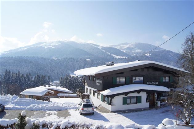 A snow-covered mountain village with traditional houses. In the background, majestic mountains rise under a clear blue sky.
