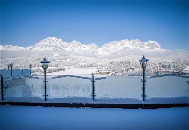 Een besneeuwd landschap met majestueuze bergen op de achtergrond. De heldere blauwe lucht zorgt voor een idyllische winteratmosfeer.