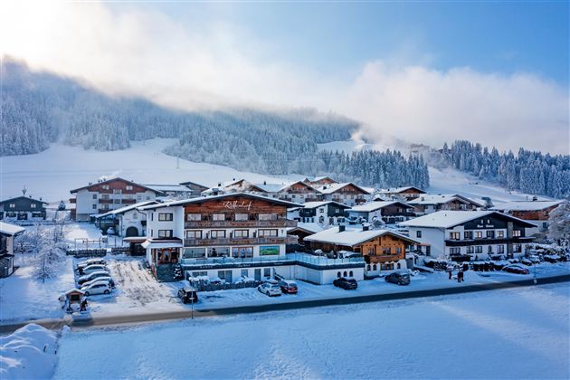 Een besneeuwd landschap met traditionele chalets en bergen op de achtergrond. De lucht is helder en de omgeving voelt rustig en uitnodigend aan.