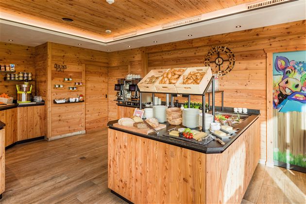 Een uitnodigende ontbijtruimte met houten panelen en een buffet vol verse gerechten. Op de tafel liggen verschillende broden, vleeswaren en fruit.