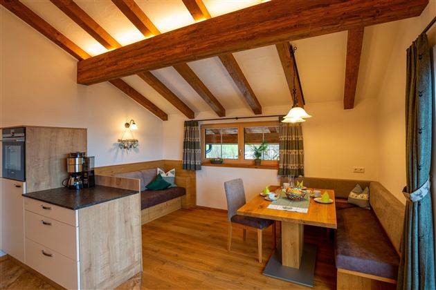 A cozy apartment with a wooden beam ceiling and modern kitchen furnishings. The dining area is inviting and bright with a view outside.
