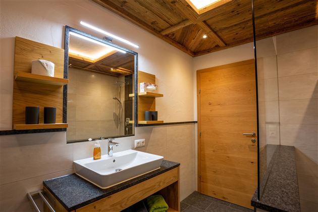 A modern bathroom with wooden shelves and a sink on a stylish base cabinet. The lighting is soft and creates a pleasant atmosphere.