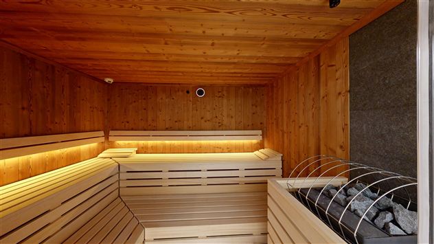 A modern sauna with wood paneling and gentle lighting. On the right side, the sauna stones are visible.