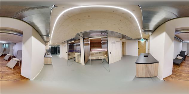 A modern wellness area with wooden saunas and cozy relaxation lounge areas. The room design is bright and inviting with soft lighting elements.