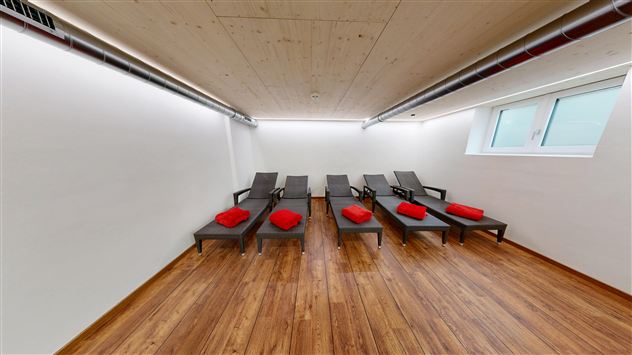 A quiet room with several loungers and red towels. The walls are bright and the floor is made of wood.