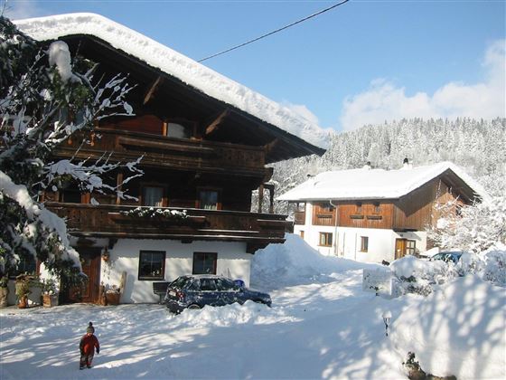 A snow-covered mountain village with traditional wooden houses.  
Children are playing in the snow in front of the houses.