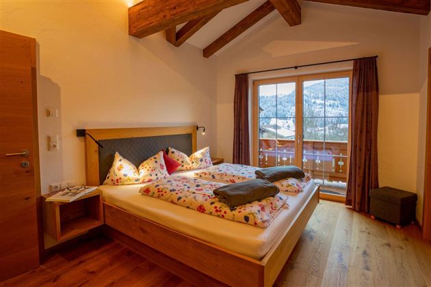 A cozy bedroom with wood paneling and a large double bed. Large windows offer a beautiful view of nature.