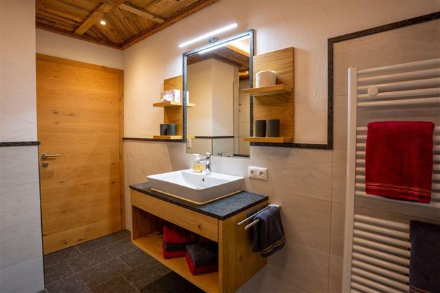A modern bathroom with wooden details and an elegant sink cabinet. The room is bright and well-lit, with towels in various colors.