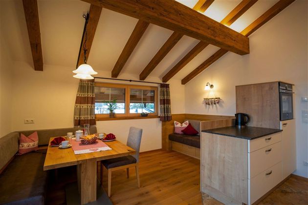 A cozy kitchenette with a dining table and seating area. Bright wooden beams give the room a warm atmosphere.