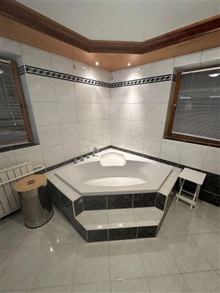 Ein modernes Badezimmer mit einer hellen, quadratischen Badewanne in der Ecke. Die Wände sind gefliest und es gibt zwei Fenster für natürliches Licht.