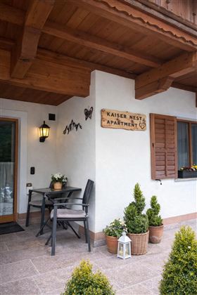 The entrance area of an apartment called "Kaiser Nest." There is a table with chairs and well-kept plants in pots.