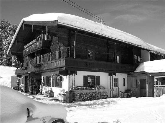 A traditional chalet in the snow with a large, sheltered roof. The wooden facade and balconies give the building a rustic charm.