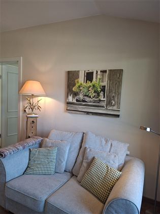 A cozy living room with a bright sofa and decorative cushions. On the wall, there is a picture featuring a window sill and plants.