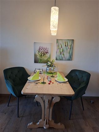An elegant dining area with a wooden table and two green chairs. On the table are decorated plates and flowers in a vase.