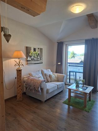 A cozy living space with a white sofa and a small table.  
Large windows let in a lot of light and provide a view outside.