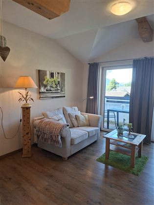 A cozy living room with a white sofa and a floor lamp. Large windows let in plenty of natural light.