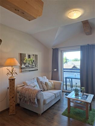 A cozy living room with a beige sofa and a floor lamp. Large windows offer a view outside and bring a lot of light into the room.