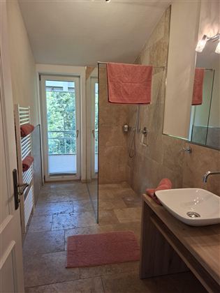 A modern bathroom with a shower and a wash basin. The walls are painted in neutral colors, and there are orange towels.