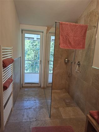 A modern bathroom with a glass shower and two windows.  
Towels in soft shades of pink are neatly arranged on a towel rack.